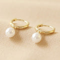Close-up of gold huggie hoop earrings with pearl drop on woman's ear&nbsp;