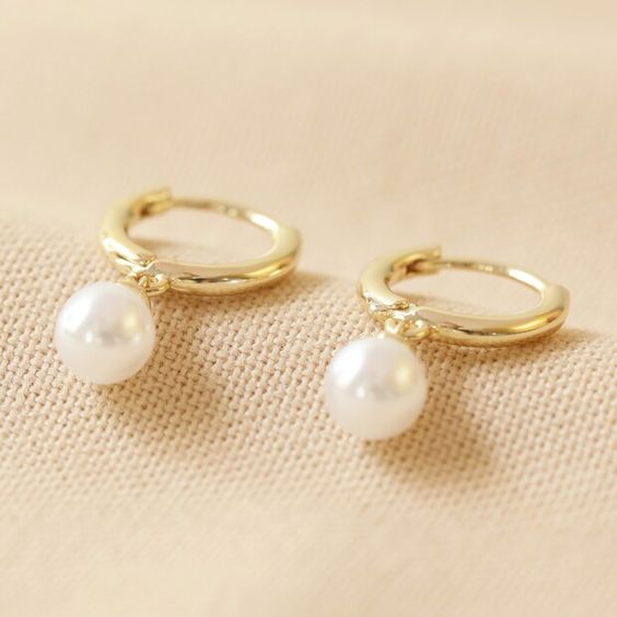Close-up of gold huggie hoop earrings with pearl drop on woman's ear&nbsp;